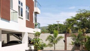 A modern building with a swimming pool, a covered outdoor area, and a view of greenery. - One Bedroom City Apartment with Pool (Kingston)