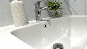 Un moderno lavabo con rubinetto cromato, un dispenser di sapone e una piccola pianta in un vaso di vetro.
