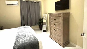 Una camera da letto con un letto, una cassettiera, una televisione a parete e una finestra con tende.