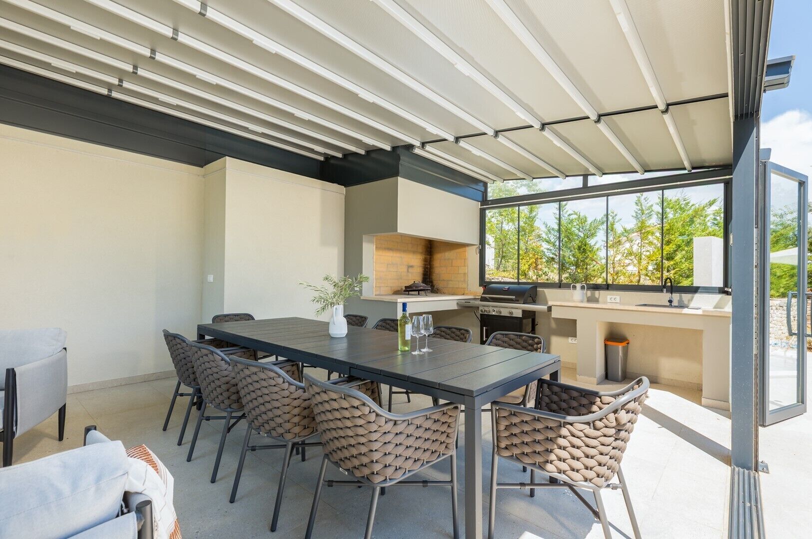 An outdoor dining area with a table and chairs, a grill, and a view of trees.