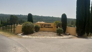 A sign reading "Les gorges de Provence" with a gravel path leading to it, surrounded by cypress trees and a fence. - Mobilhome des gorges du verdon (Montagnac-Montpezat)