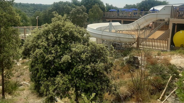 A water park with a large water slide, wooden deck, and surrounding greenery. - Mobilhome des gorges du verdon (Montagnac-Montpezat)