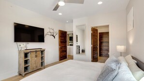 Une chambre avec un grand lit, un téléviseur fixé au mur, une armoire en bois et un ventilateur de plafond.