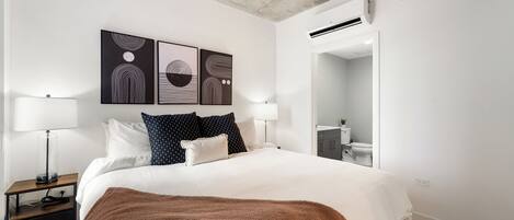 A modern bedroom with a large bed, two bedside tables, a brown throw blanket, and abstract wall art.