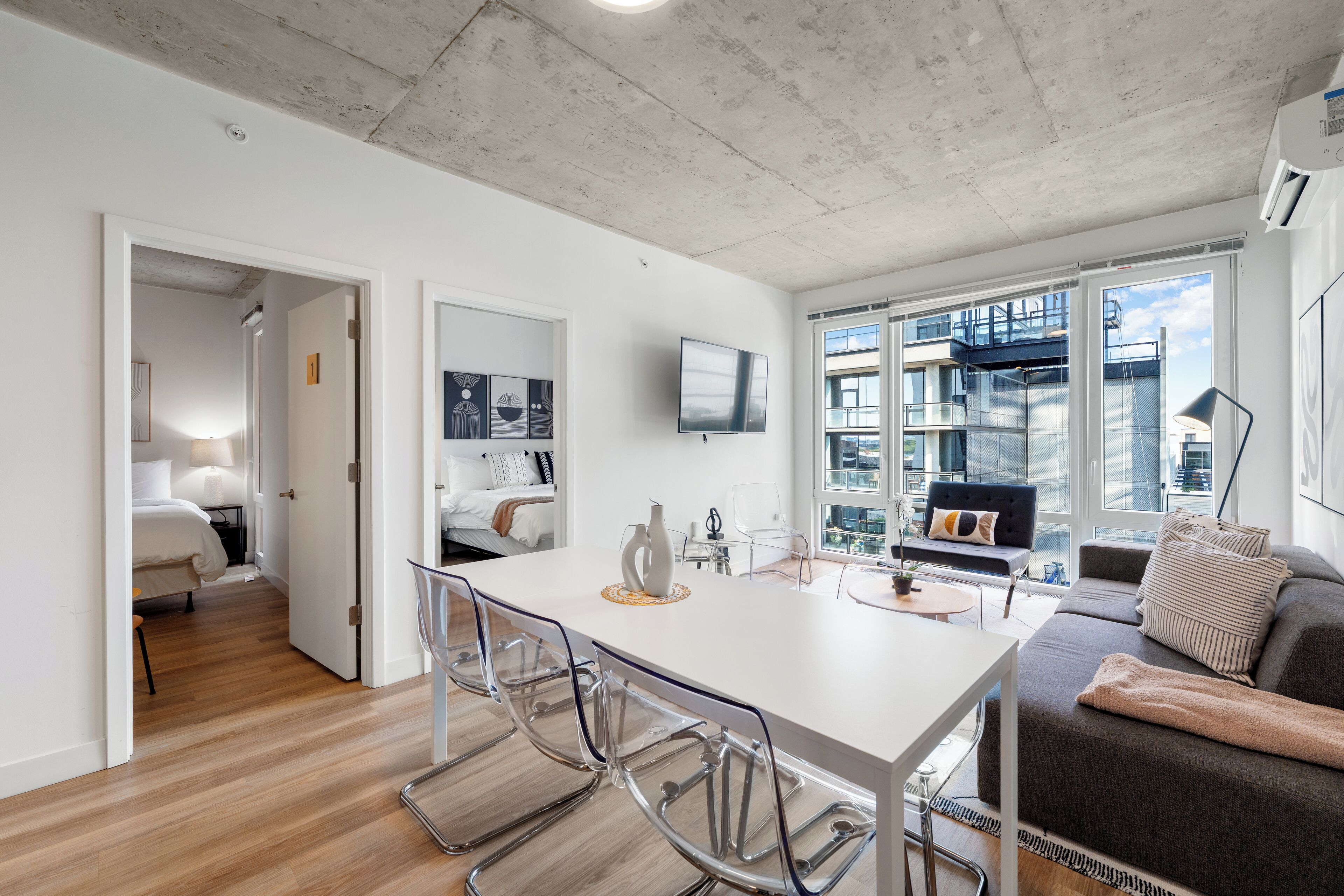 Un espacio habitable moderno con comedor, sofá y vista a un paisaje urbano a través de grandes ventanales.