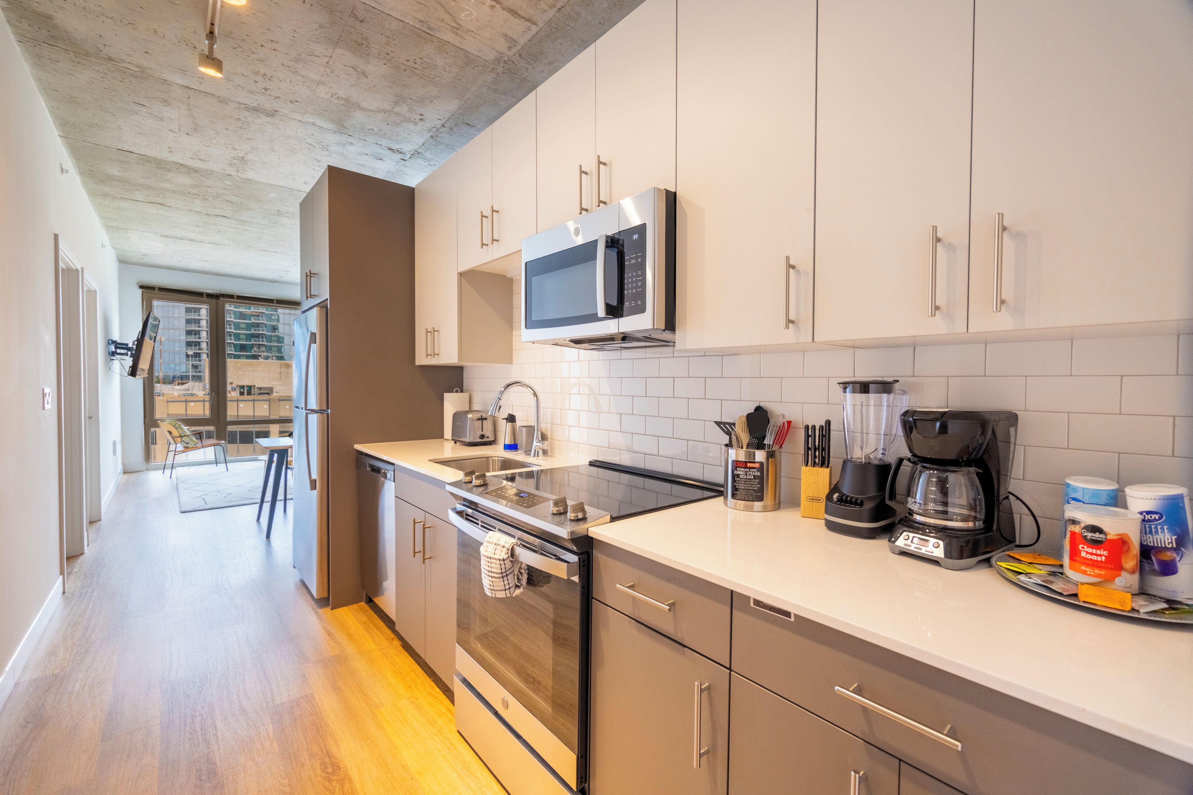 Una cocina moderna con electrodomésticos de acero inoxidable, armarios blancos y un comedor visible con una mesa y sillas.