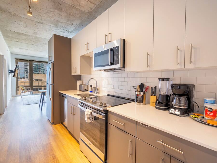 Una cocina moderna con electrodomésticos de acero inoxidable, armarios blancos y un comedor visible con una mesa y sillas.