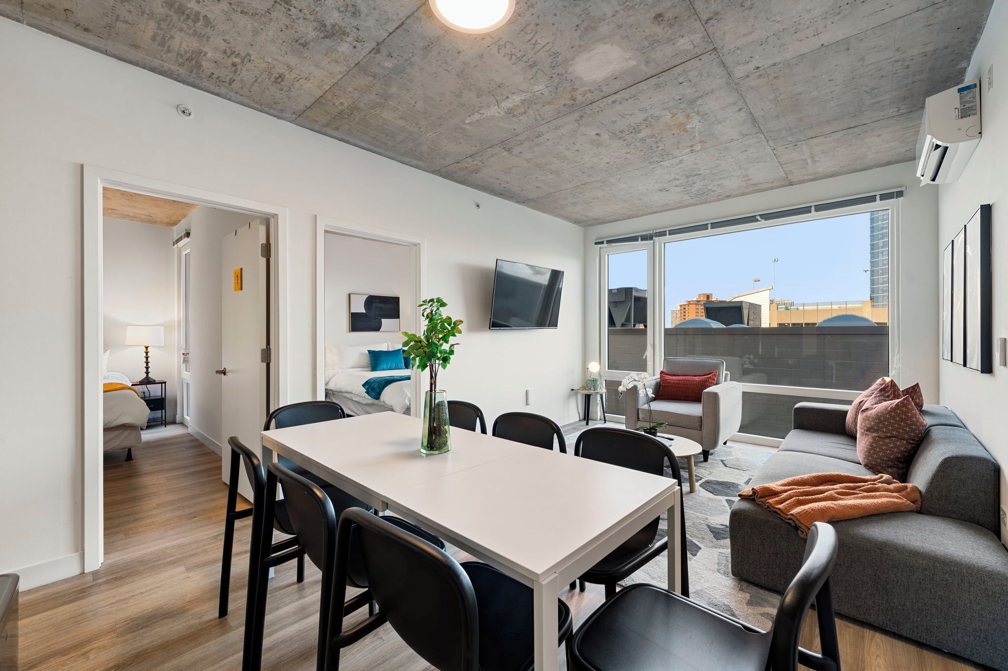 Un apartamento moderno con comedor, sala de estar con sofá y televisión, y un amplio ventanal con vista a la ciudad.