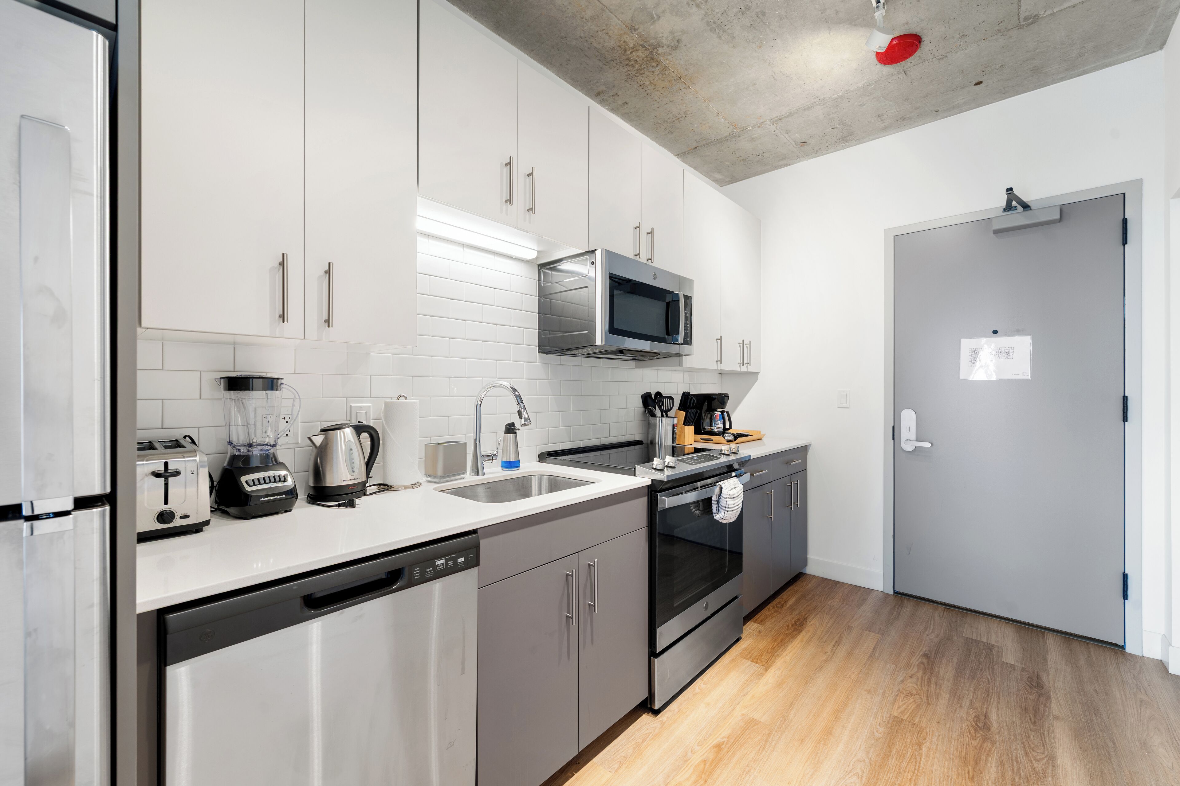 A modern kitchen with stainless steel appliances, white cabinetry, and a wooden floor.