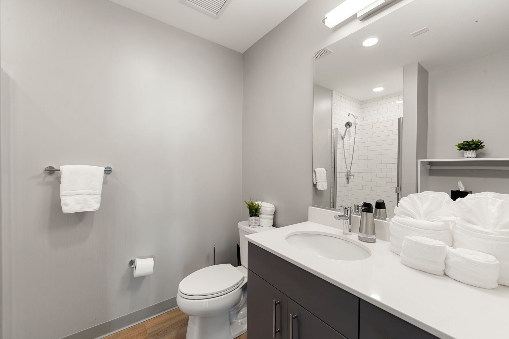 Une salle de bain moderne avec des toilettes blanches, un lavabo avec un miroir au-dessus et un espace douche.