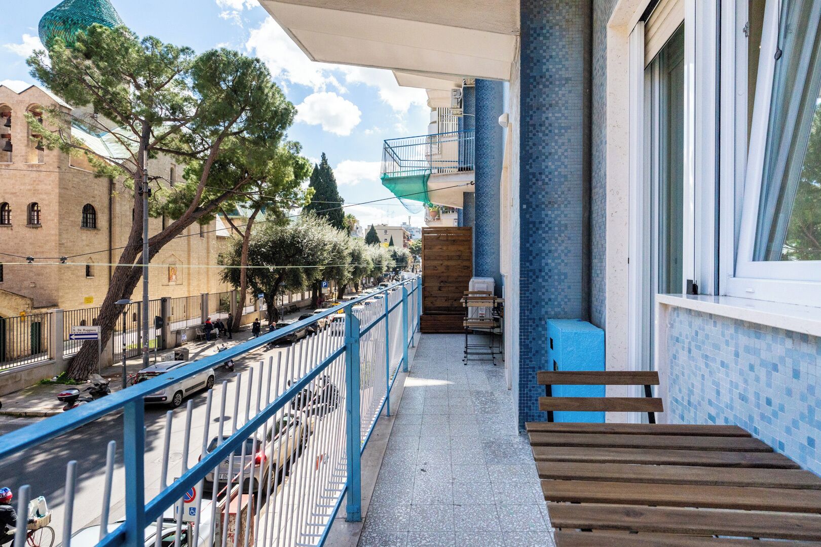 Un balcon donnant sur une rue, un banc en bois et une table.