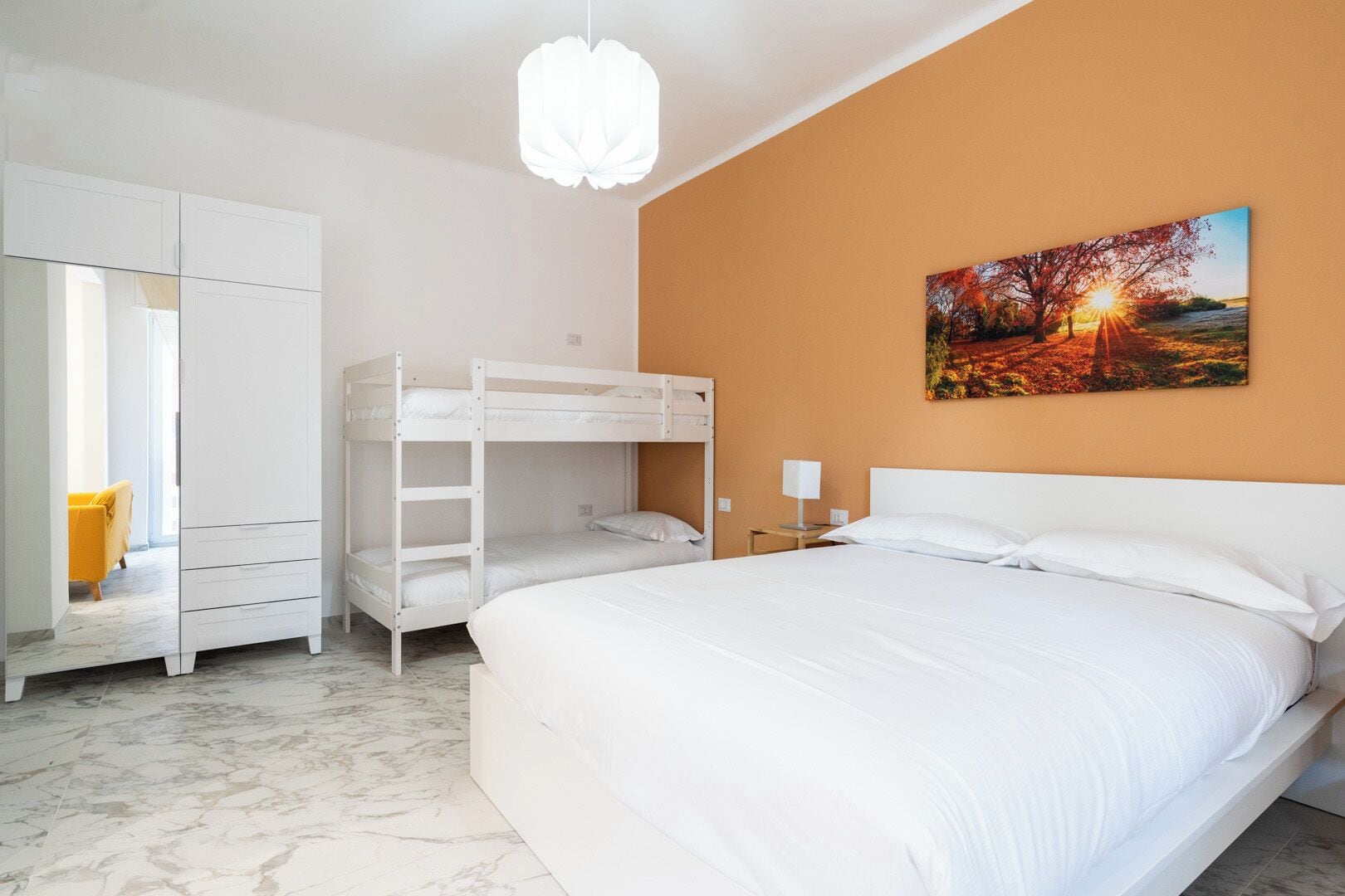 A bedroom with a bunk bed, a wardrobe, a bedside table with a lamp, and a painting on the wall.