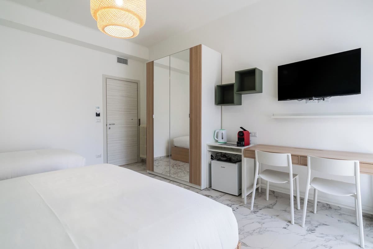 A hotel room with a bed, a desk with a chair, a television, and a mirror.