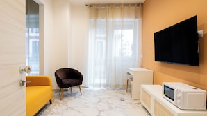 A modern hotel room with a yellow sofa, a dark armchair, a small desk, a television, and a microwave. - Saint Nicholas House by Wonderful Italy (Bari)