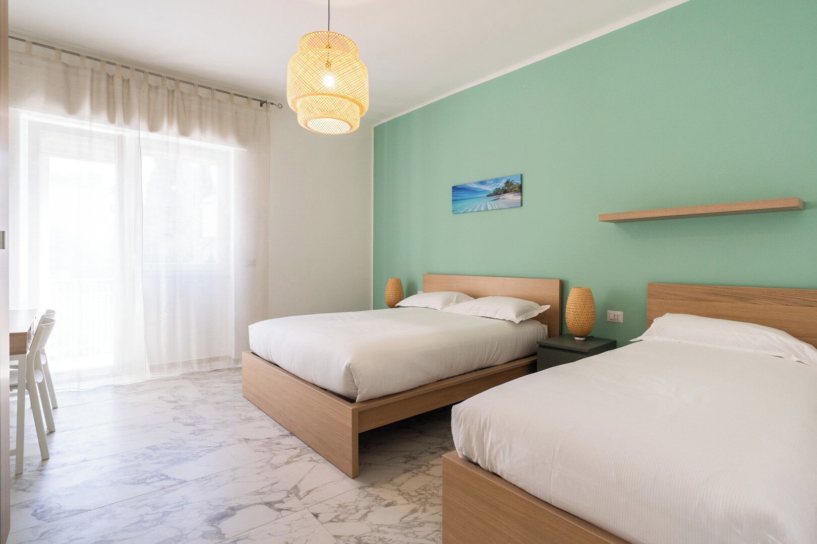 A bedroom with two beds, a dining area, and a large window with sheer curtains.