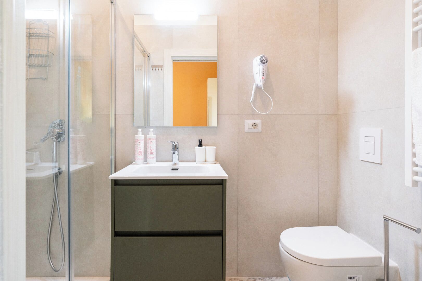 Un baño moderno con cabina de ducha de vidrio, un lavamanos blanco con artículos de aseo y un inodoro.