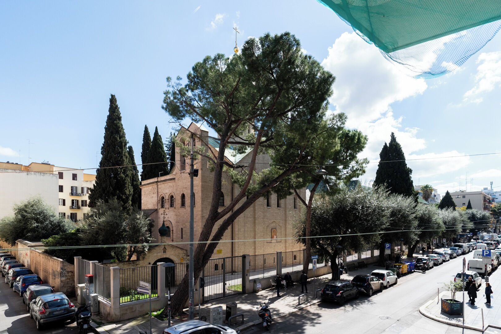 A church with a tall bell tower, surrounded by parked cars and trees.