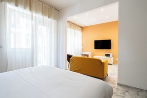 Ein Hotelzimmer mit einem großen Bett, einem gelben Sessel, einem an der Wand befestigten Fernseher und einer kleinen weißen Kommode.