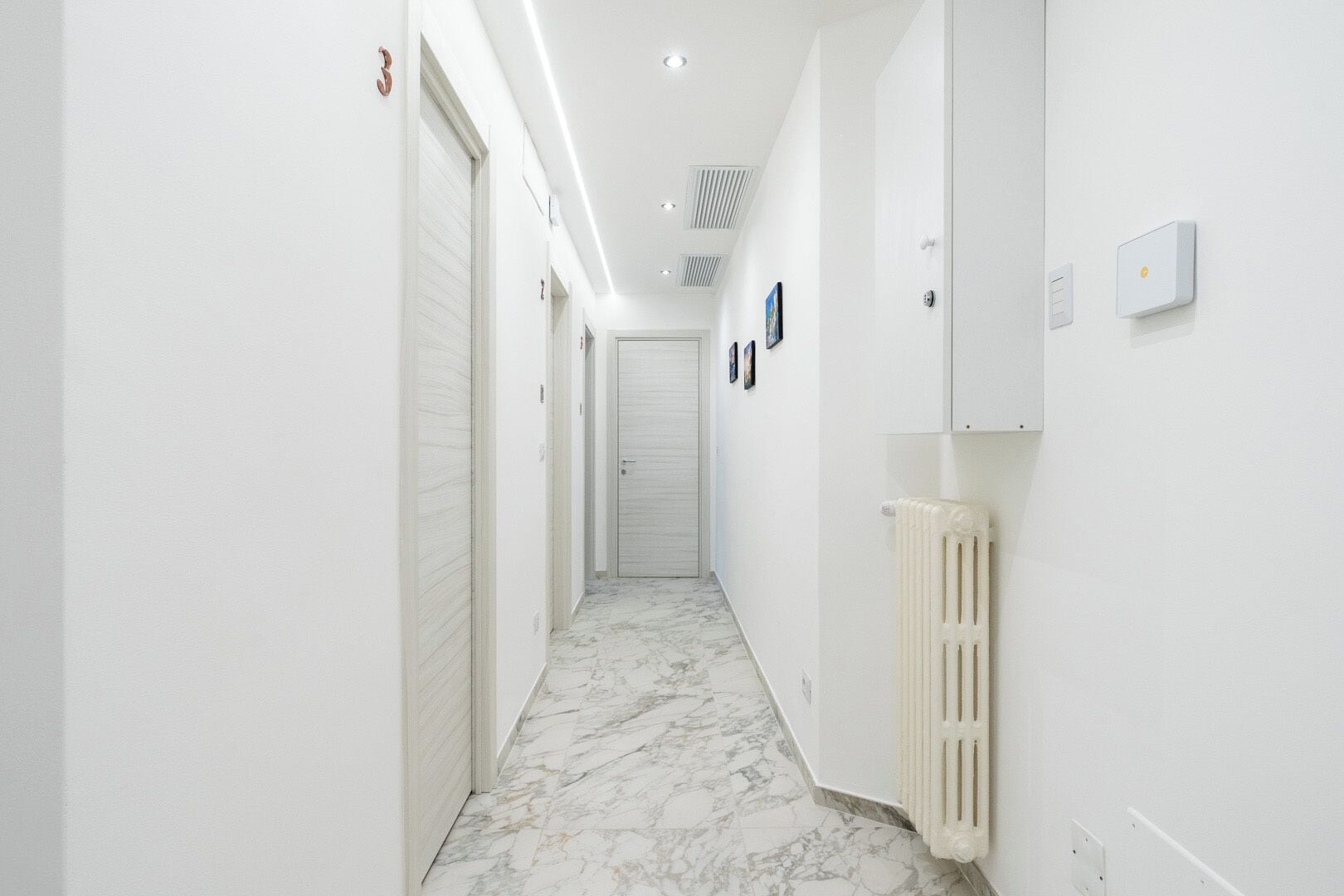 A hallway with white walls, a marble floor, and a radiator.