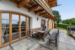 A building with large windows, wooden beams, and a patio area with benches and a table. - Apartment 'Walcher Alm' with Lake View, Shared Terrace and Wi-Fi (Höslwang)