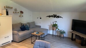 Uma sala de estar moderna com um sofá, uma mesa de centro, uma televisão e plantas decorativas.