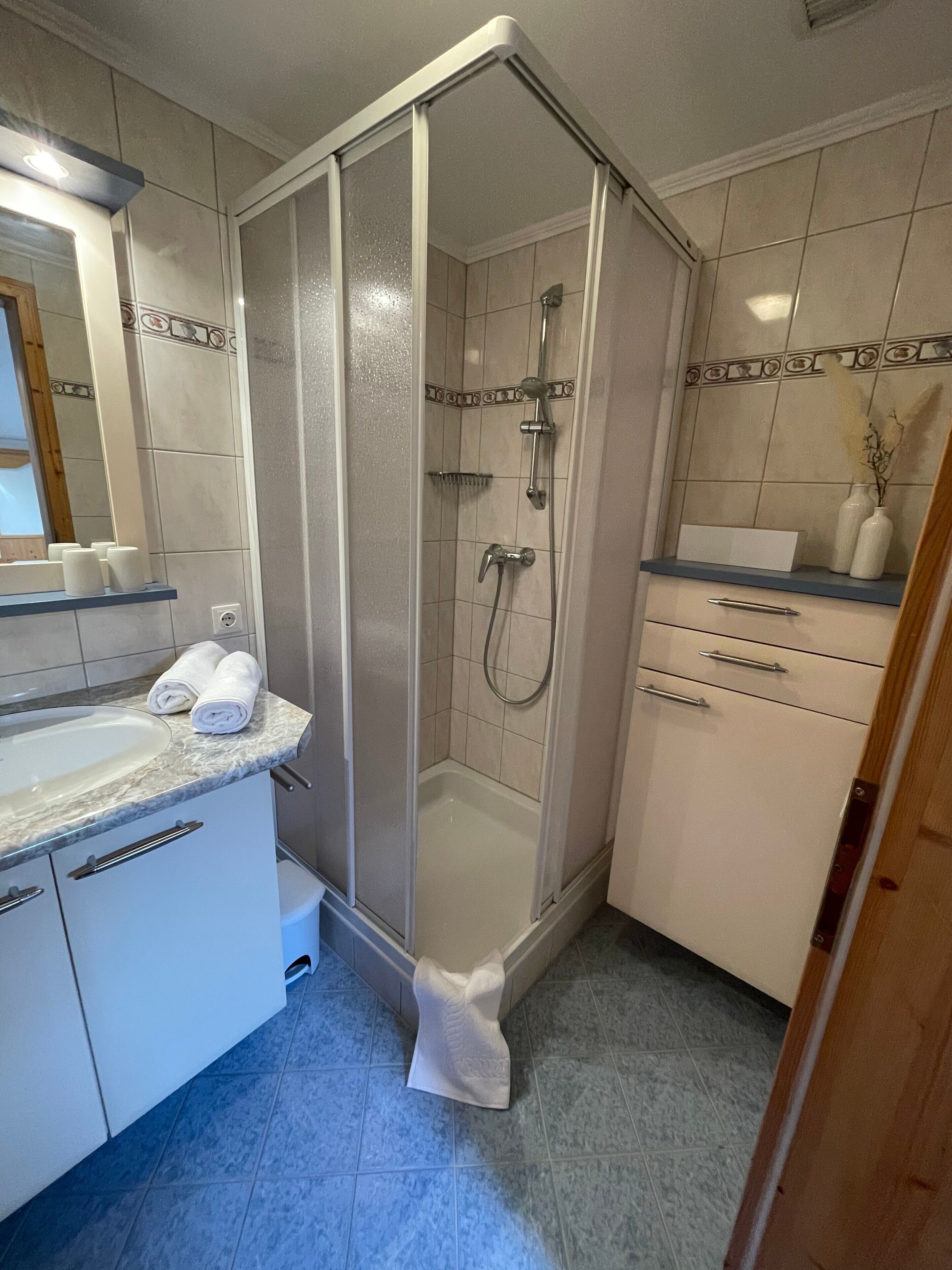 A bathroom with a glass-enclosed shower, a sink with a marble countertop, and white cabinets.