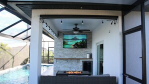 Un espacio exterior moderno con piscina, chimenea y un televisor grande montado en una pared de piedra.