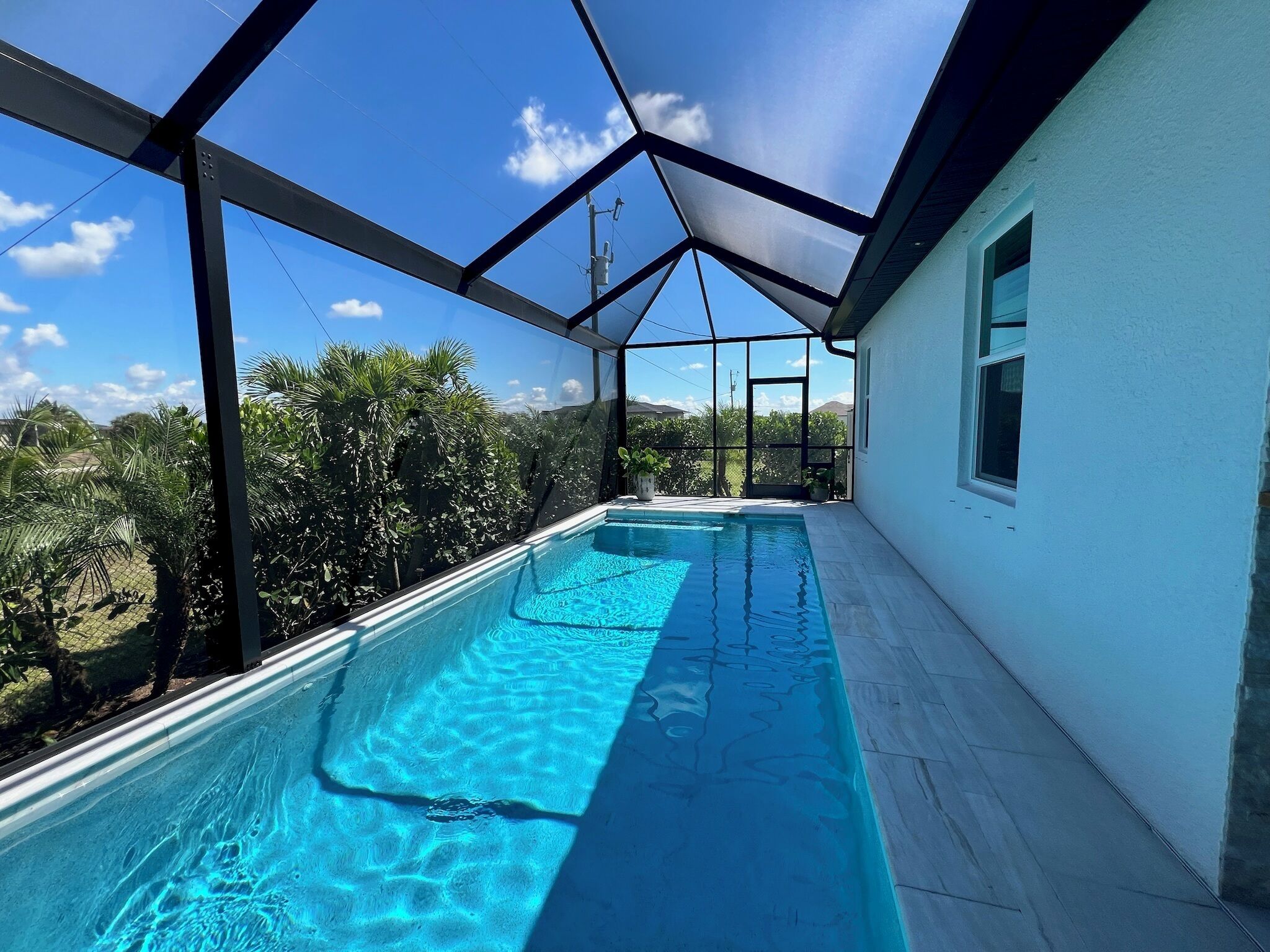 A swimming pool with a glass ceiling, surrounded by greenery and a clear sky.