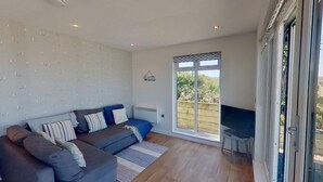 A spacious living room with a grey sofa, a small TV table, and a large sliding glass door leading to a garden.