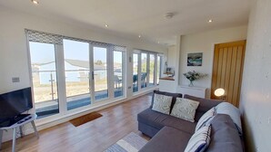 A spacious living room with a large window, a sofa, a TV, and a wooden floor.