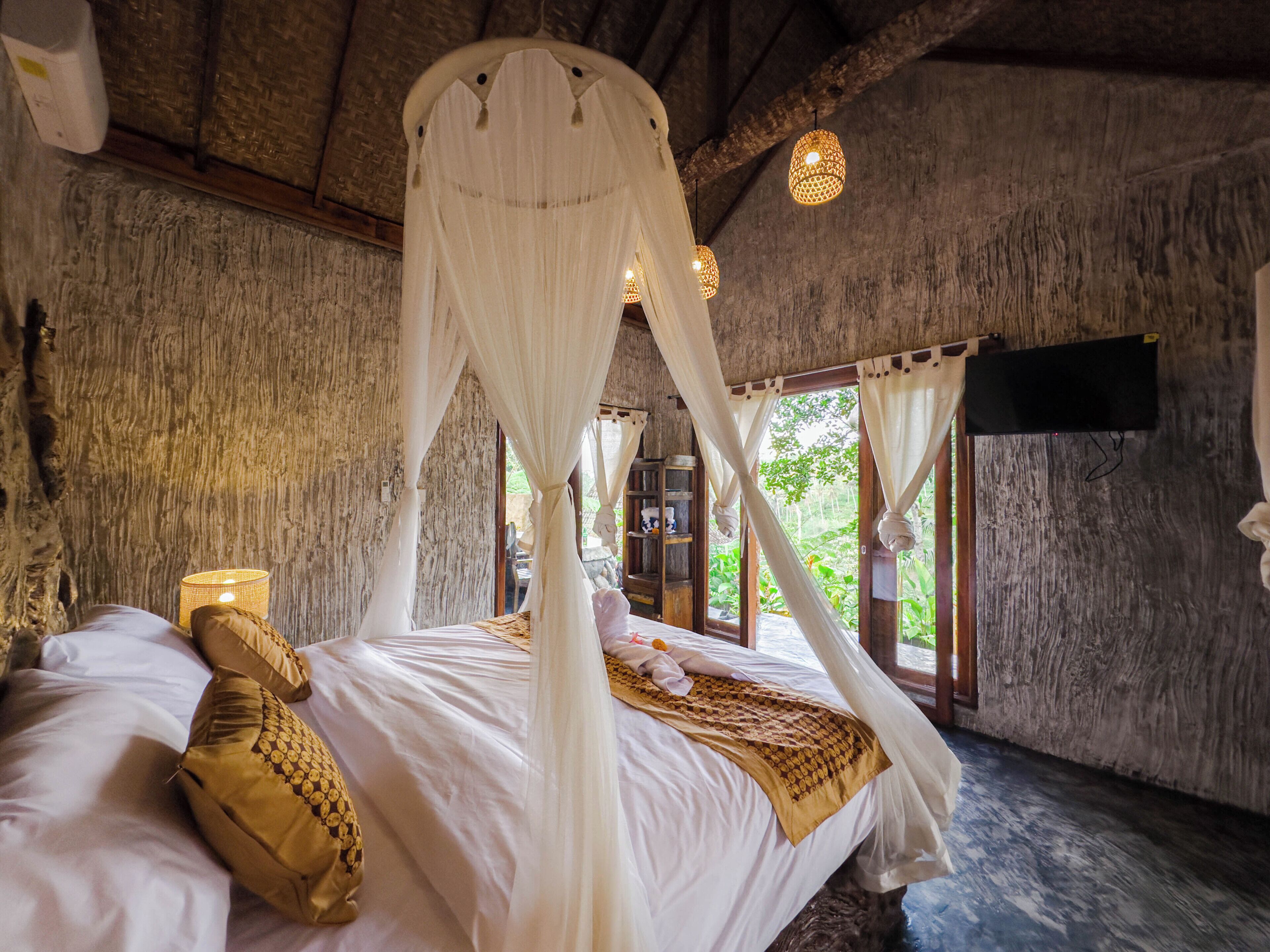 Une chambre à coucher avec un lit à baldaquin, une tête de lit en bois et une grande fenêtre avec des rideaux.