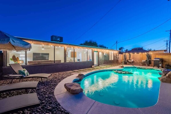 A modern outdoor pool area with a lounge chair and a small waterfall feature. - Spacious 5BR Retreat + Game Room (Phoenix)