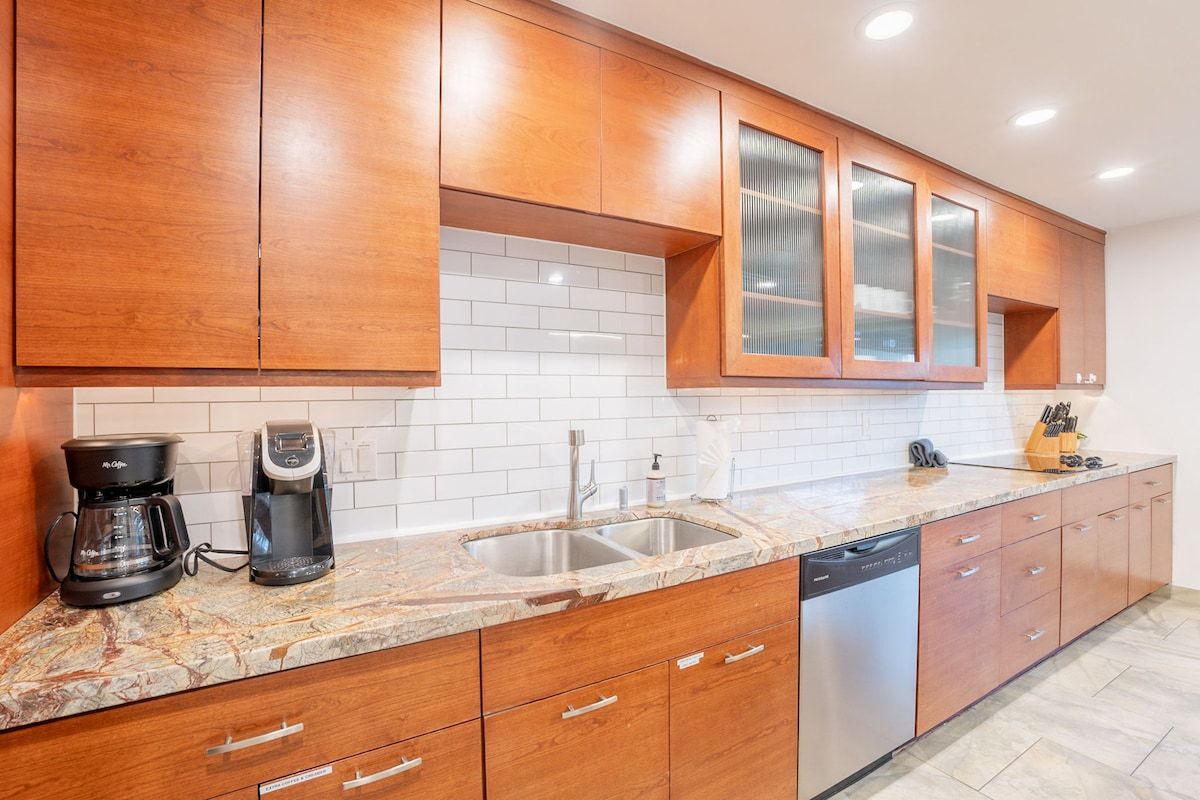 A kitchen with wooden cabinets, a granite countertop, a coffee maker, a dishwasher, and a sink.