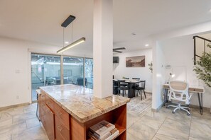 A modern kitchen with a marble countertop, wooden cabinets, and a dining area with a table and chairs.