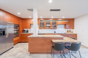 A modern kitchen with wooden cabinets, a stainless steel refrigerator, a granite countertop island, and two black chairs. - Old Town Living • Walk to Dining, Bars & Fun (Scottsdale)