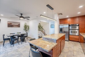 A modern kitchen with a marble countertop, stainless steel appliances, and a dining area with a table and chairs.