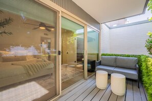 A modern bedroom with a sliding glass door leading to a balcony, a grey sofa, and two round side tables. - Old Town Living • Walk to Dining, Bars & Fun (Scottsdale)
