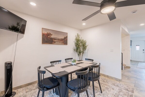 A dining area with a table, chairs, a ceiling fan, a TV, and a painting on the wall. - Old Town Living • Walk to Dining, Bars & Fun (Scottsdale)