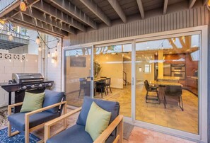 Eine Außenpatio mit Grill, Sitzbereich und Glastüren, die in eine Küche führen.