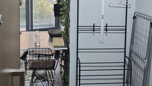 A room with a dining table, chairs, a wall-mounted drying rack, and a window with a view of buildings. - Charming Batumi Apartment With City and Water Views (Batumi)