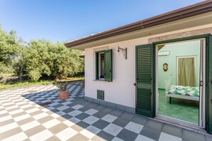 Una habitación con suelo a cuadros, una cama con colcha verde y una ventana con contraventanas verdes.