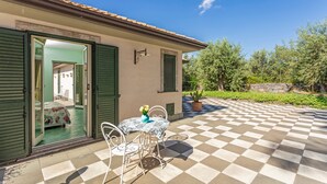 A villa with a checkered patio, a dining area with a table and chairs, and a view of the interior through open doors. - Bed and Breakfast 'Sole' with Sea View, Shared Pool and Wi-Fi (Calatabiano)