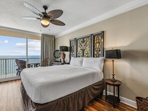 A hotel room with a large bed, a ceiling fan, a view of the ocean, and decorative wall art.