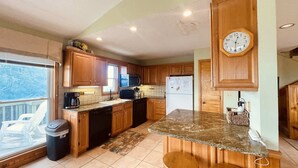 A kitchen with wooden cabinets, a granite countertop, a refrigerator, a microwave, and a clock on the wall. - TM-2  Cox Retreat Amazing 6-Bedroom Hot Tub (Beech Mountain)