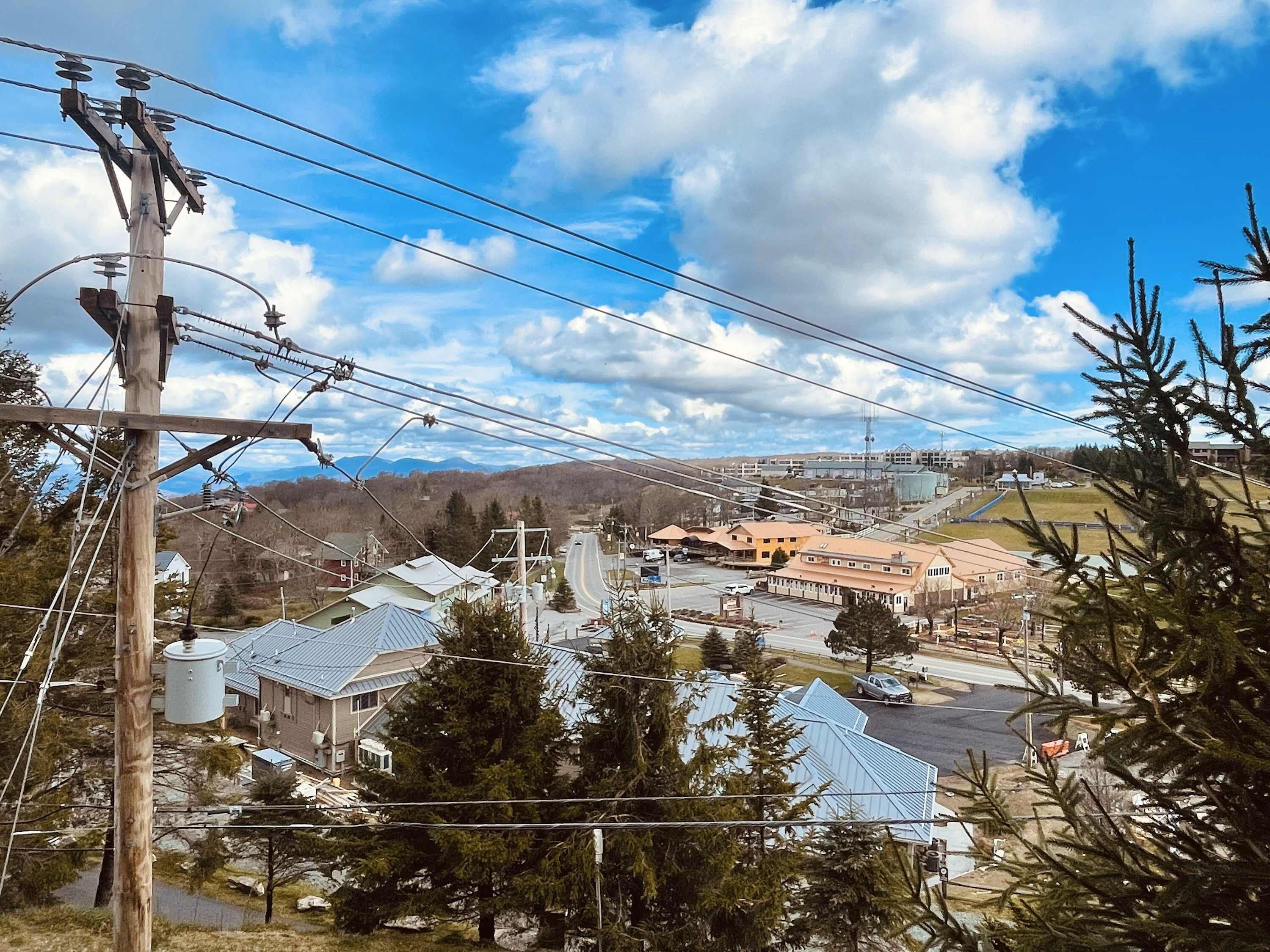 Eine Stadt mit einem markanten Strommast, Wohnhäusern und einer Straße, die zu einem entfernten Gebirge führt.