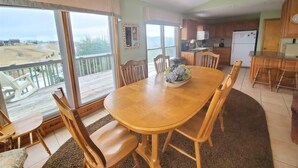 A dining area with a wooden table and chairs, a kitchen in the background, and a view of a balcony with outdoor furniture. - TM-2  Cox Retreat Amazing 6-Bedroom Hot Tub (Beech Mountain)