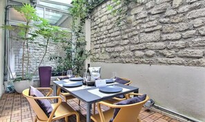 An outdoor dining area with a stone wall, potted plants, and a table set for two. - A QUINTESSENTIAL PARISIAN EXPERIENCE WITH PRIVATE TERRACE ,AIR CON-SAINT GERMAIN (Paris)