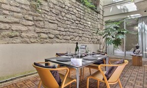 An outdoor dining area with a stone wall, a Buddha statue, and a view of a building through a glass door.