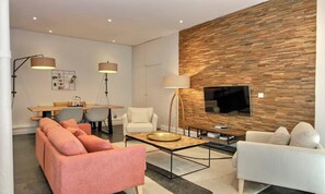 A modern living room with a sofa, armchair, coffee table, and a flat-screen TV mounted on a wooden wall.