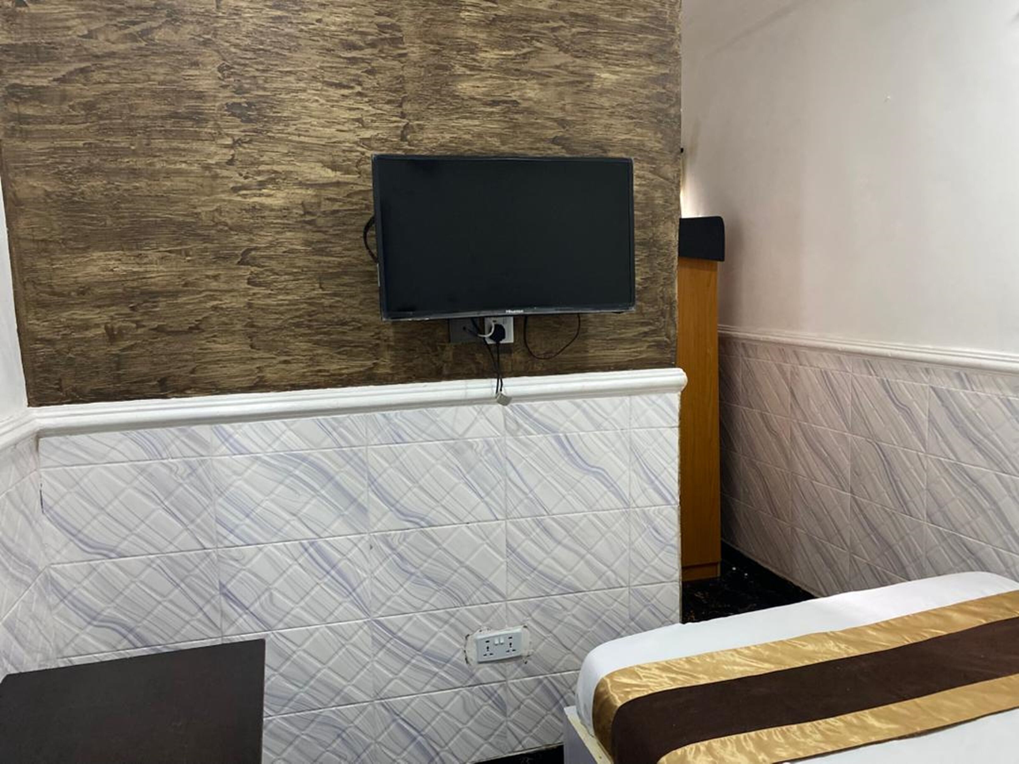 Hotelkamer met een houten accentmuur, een wandmontage televisie, muren met een marmerpatroon en een bed met een bruin en gouden sprei.